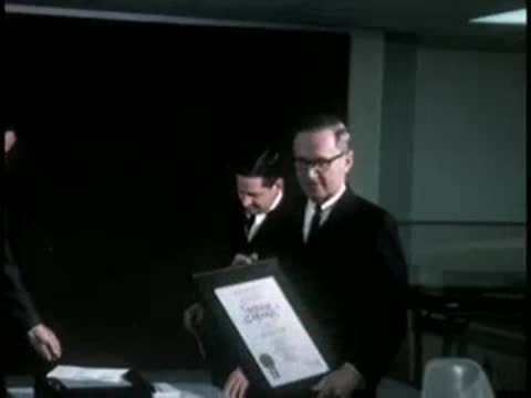Presentation of a framed certificate by men in suits