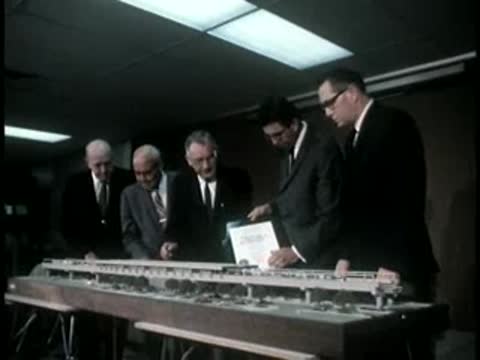Group of men in suits gathered around a transit model