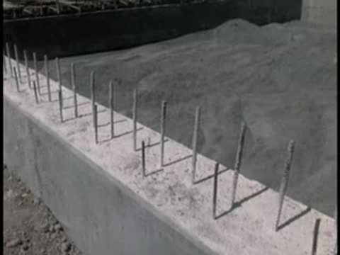 Close-up of concrete foundation edge with vertical rebar spikes, construction site.