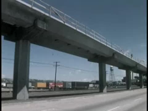 Low angle tracking shot driving under elevated highway viaduct and pillars.