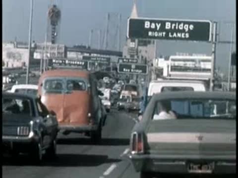 Cars driving on highway approaching overhead sign for Bay Bridge.