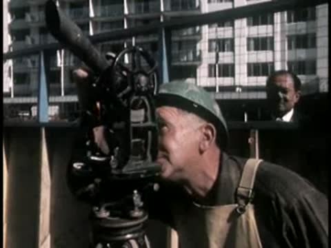 Construction worker operating surveying equipment at a building site.