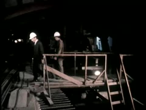 Two construction workers in hard hats walking on wooden staging.