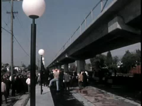 Outdoor ribbon cutting ceremony under elevated highway with crowd.