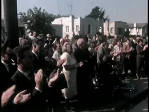 Large crowd applauding outdoors during a daytime event.