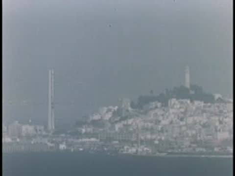 Distant hazy view of hills and water with a tall structure in the morning light.