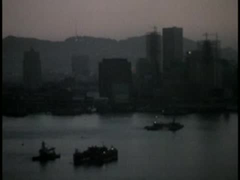 Harbor view at dusk with boats and city skyline silhouettes in the background.
