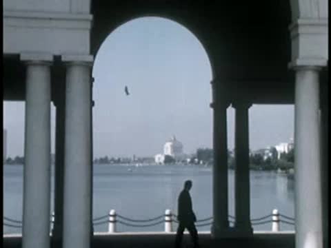 Water view through architectural archways with person walking in distance.
