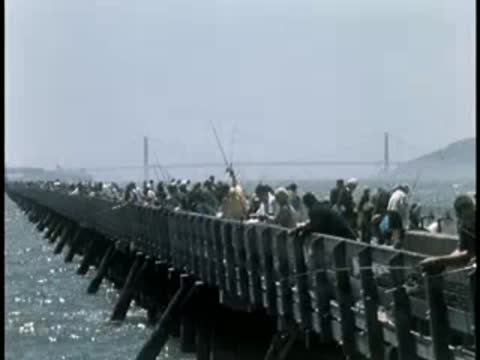 Crowded wooden pier extending over water with people fishing.