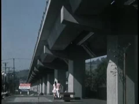 Underneath a concrete highway overpass with figures walking.