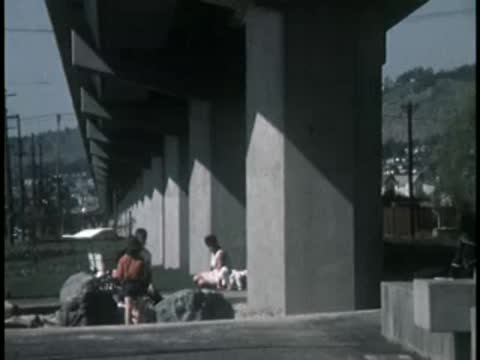 People relaxing and walking near concrete pillars under an overpass.