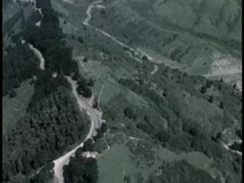Aerial view of a winding road through a green, hilly landscape.