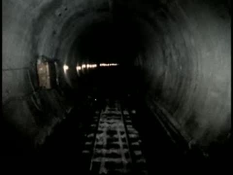 View from inside a dark railway tunnel with faint lights.