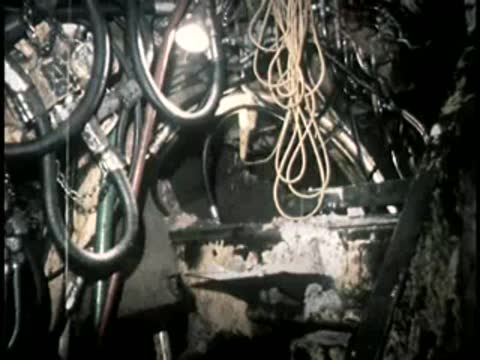 Cables and equipment hang from the ceiling of an active underground excavation site.