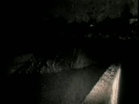 A dark underground passageway with concrete walls illuminated by a dim light.