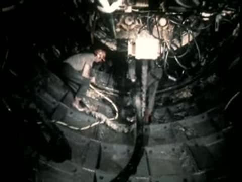 A worker manipulates equipment inside a tight, curved underground construction shaft.