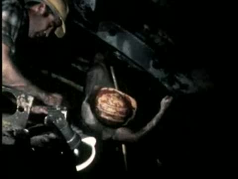 A worker interacts with equipment while another supervises inside a dark tunnel setting.