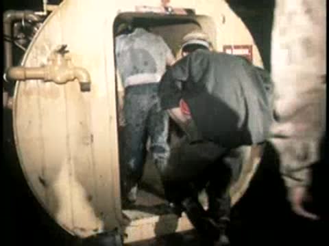 Workers exit a circular hatch or airlock door into an underground space.