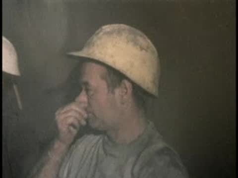 A worker wearing a hard hat rests his face inside a smoky tunnel environment.