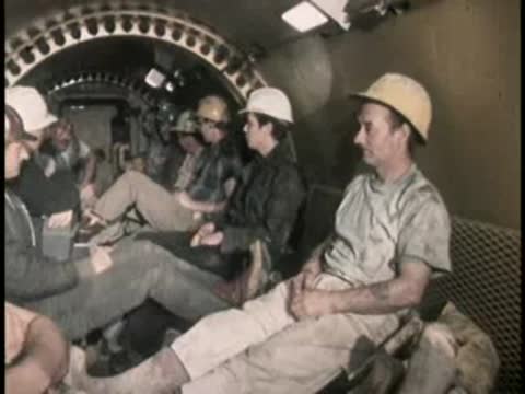 Several workers sit together inside a train or transport vehicle underground.
