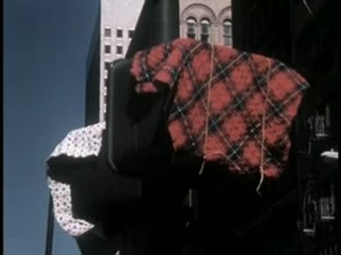 A person carrying a plaid blanket walks along a busy city sidewalk.