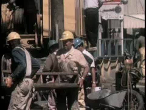 Construction workers in hard hats collaborate on a street-level project.