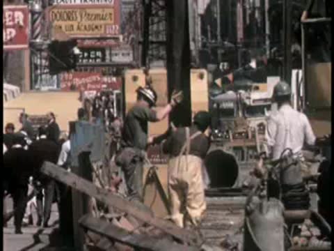 Workers manage heavy equipment on a busy urban street with storefronts visible.