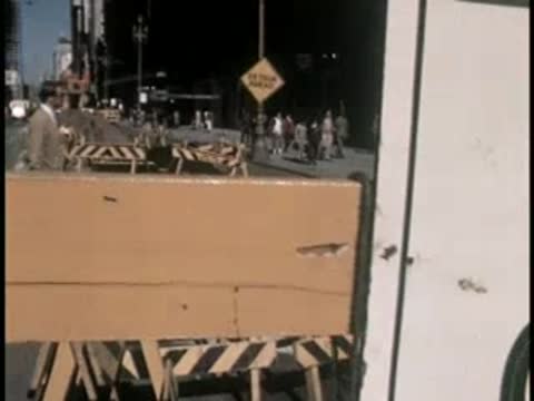 A road closed sign is positioned near street barricades in a busy city area.