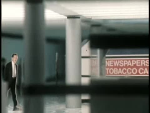 Commuters walk past supporting pillars inside a spacious underground station platform.