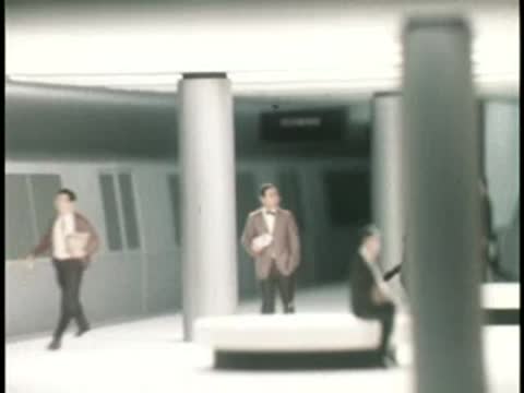 Commuters wait and walk on a brightly lit modern subway station platform.