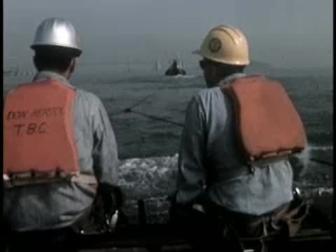 Two workers wearing life jackets and hard hats looking out over the water.