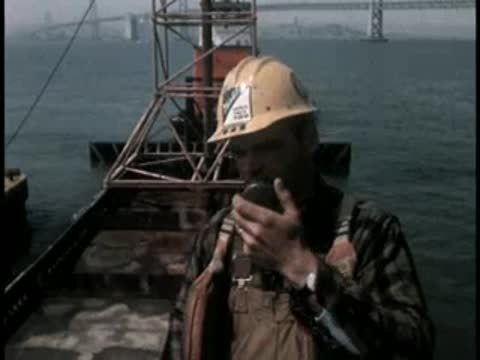 Construction workers and tugboats operating around a floating platform structure.