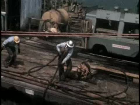 Workers handling cables and equipment on the deck of a construction barge.