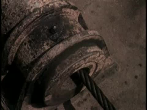 Close-up of a heavy metal cable running through a mechanical winch guide.