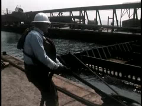 Worker in a hard hat pulling on a heavy rope or cable outdoors.