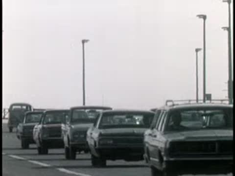 Rear view of classic cars driving along a multi-lane highway in the 1960s.
