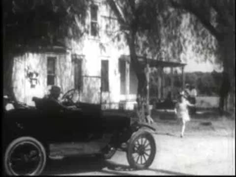 a vintage car parked outside a house with children playing nearby