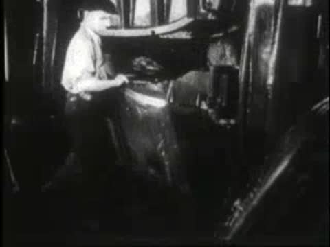Workers assembling car body panels inside a busy manufacturing plant.
