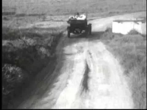 a vintage car driving away along a dirt road