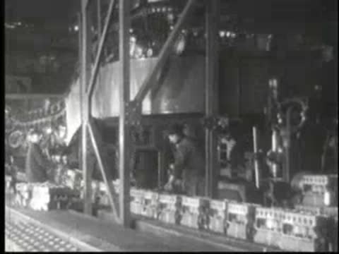 Workers operating assembly machinery on a production floor in a factory.