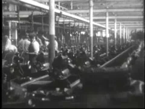 Long perspective view of an active factory floor with numerous workers and machines.