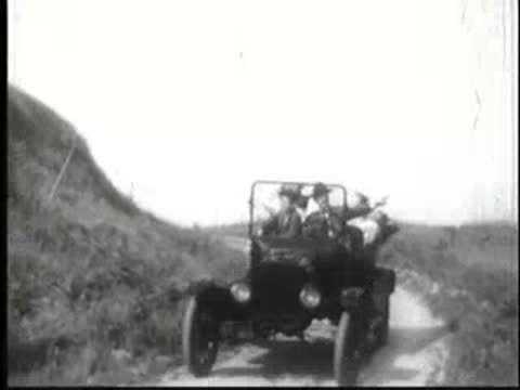 vintage cars driving towards the camera on a dirt road