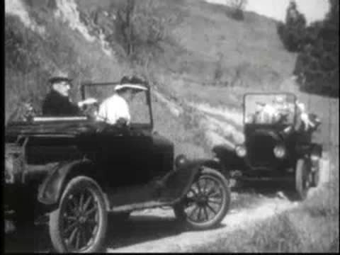 vintage cars following each other on a dirt road