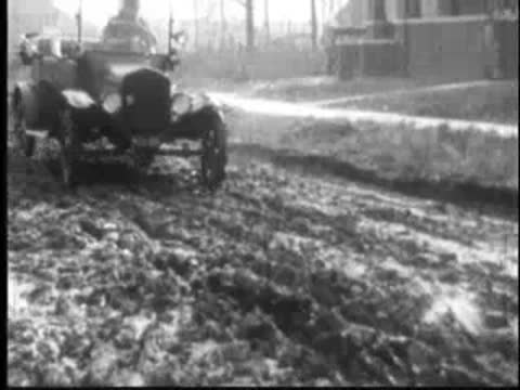 a vintage car driving across a muddy field