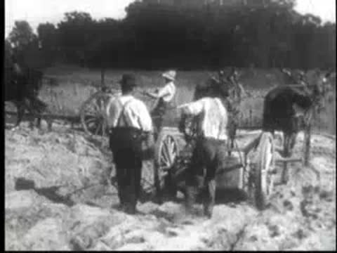 Men working with horses and equipment on dirt road in early 20th century.