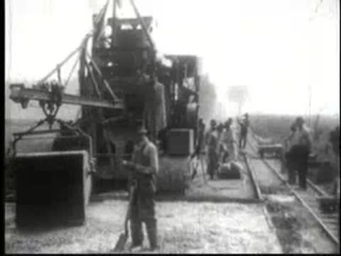 Heavy road roller machine working on surface with man standing nearby.