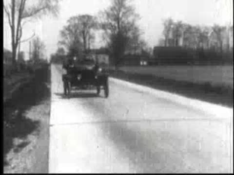 Vintage cars driving away along a paved rural road.
