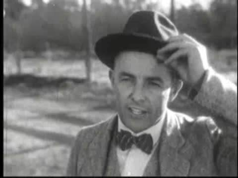 Man in fedora and bow tie smiling and adjusting his hat.