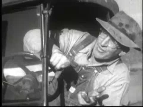 Man leaning into vehicle cabin pointing downward with animated expression.