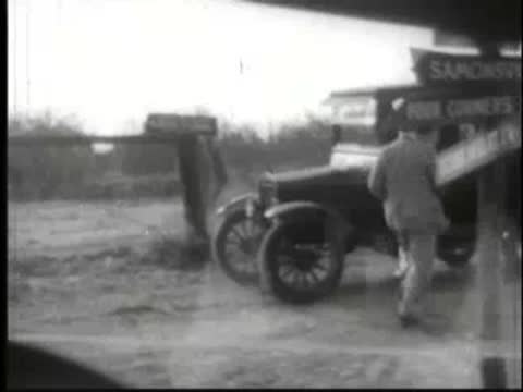 Man in suit running away from parked car past signpost.